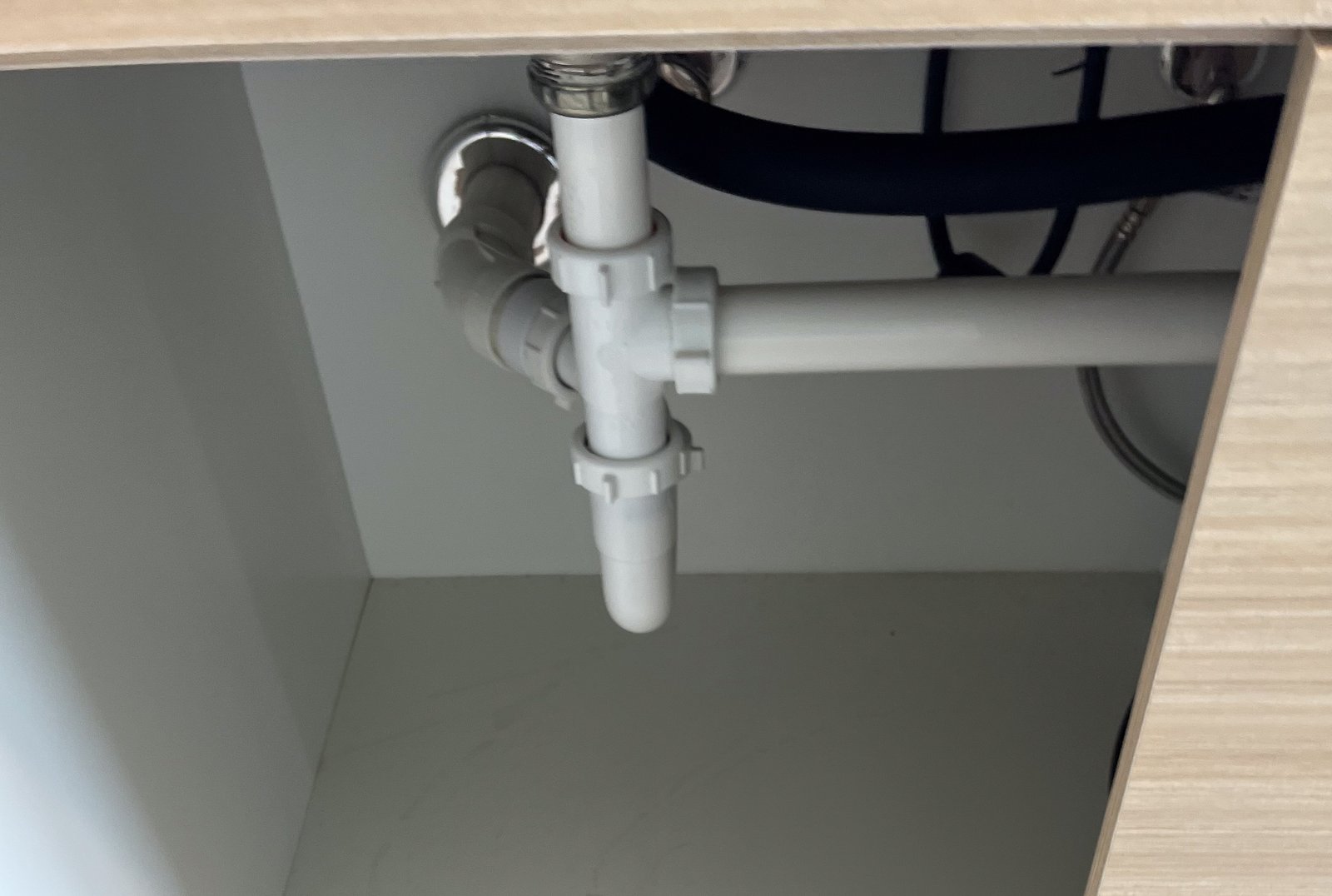 PVC drain pipes and water connections inside an open under-sink cabinet
